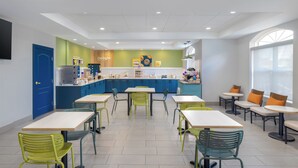A modern dining area with multiple tables and chairs, a kitchen counter, and a large window providing natural light.