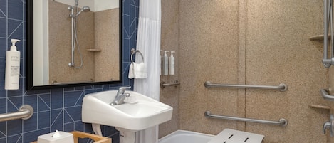 Un baño moderno con ducha, lavabo y bañera, equipado con barras de apoyo y un perchero para toallas.