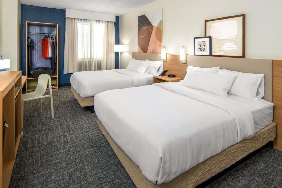 Een hotelkamer met twee bedden, een bureau, een stoel, een kledingkast en kunstwerken aan de wanden.