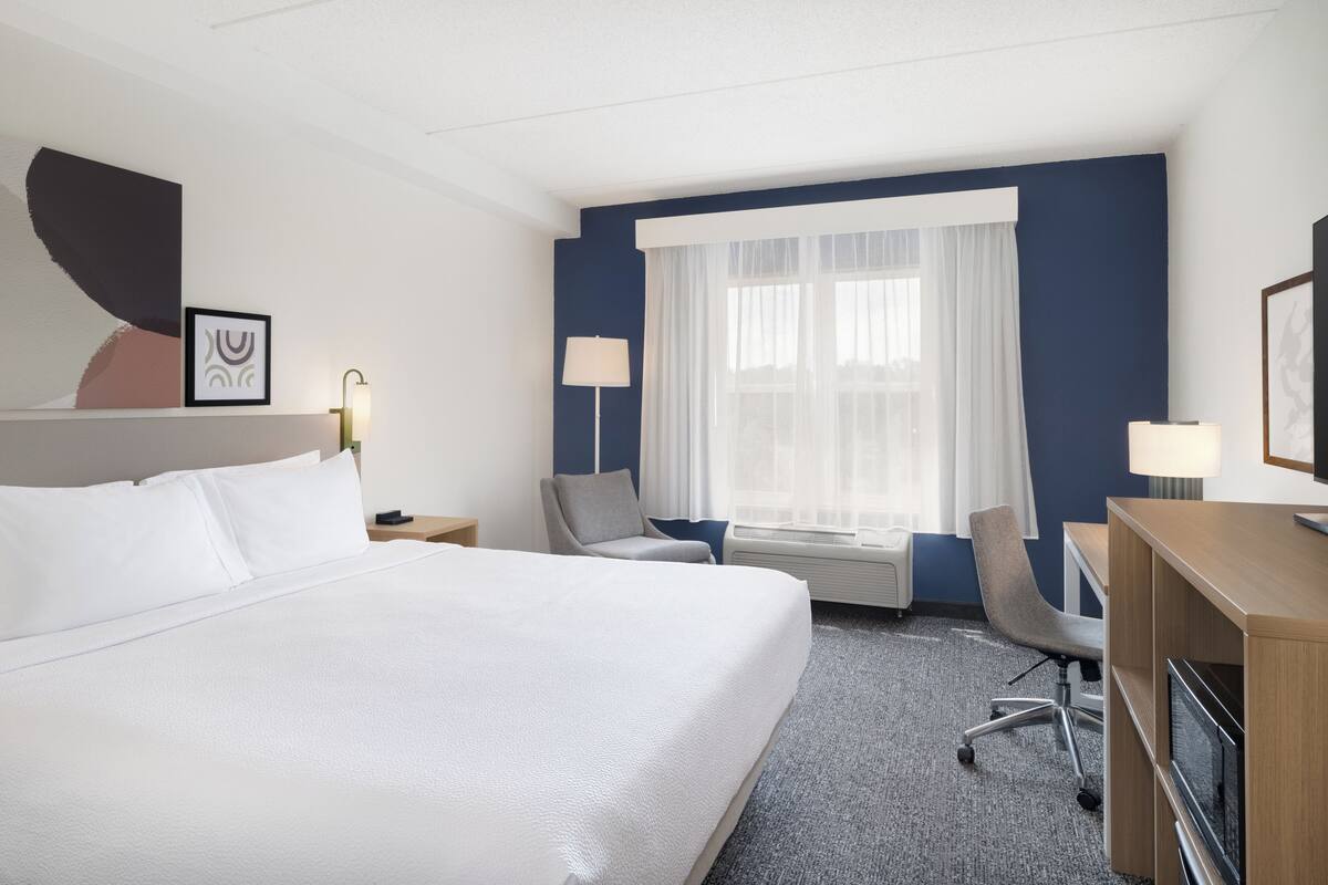 Een hotelkamer met een groot bed, twee stoelen, een bureau en een raam met gordijnen.