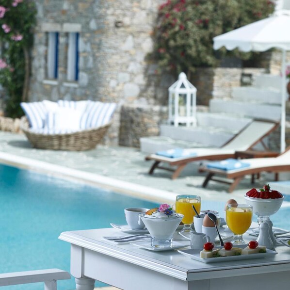 A poolside breakfast setup with a table, breakfast items, and a view of the pool and lounge chairs.