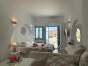 A bedroom with two beds, a sitting area, a TV, and a balcony with a view. - Folegandros Apartments (Folegandros)
