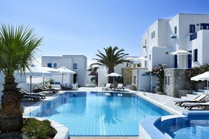 A swimming pool with lounge chairs and umbrellas, surrounded by white buildings with blue accents.