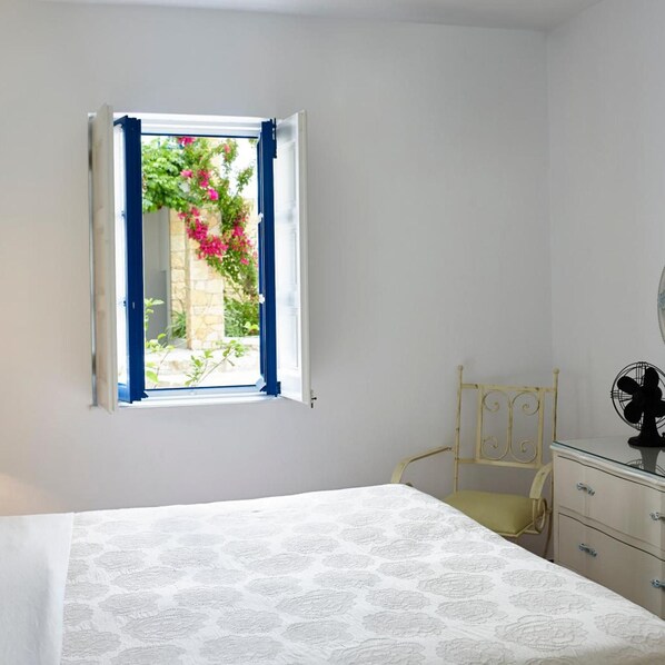 A bedroom with a bed, a chair, a dresser, and a window with blue curtains.