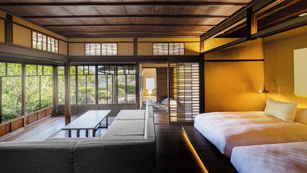 Una habitación tradicional japonesa con suelo de tatami, una mesita baja y una cama con ropa de cama blanca.