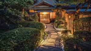 Una casa japonesa tradicional con tejado de tejas, una puerta de madera y un camino de piedra que conduce a la entrada.