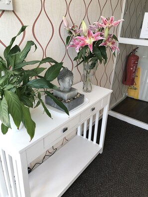 Une console blanche ornée d’une statue de Bouddha, d’un vase contenant des lys roses et d’une plante en pot.