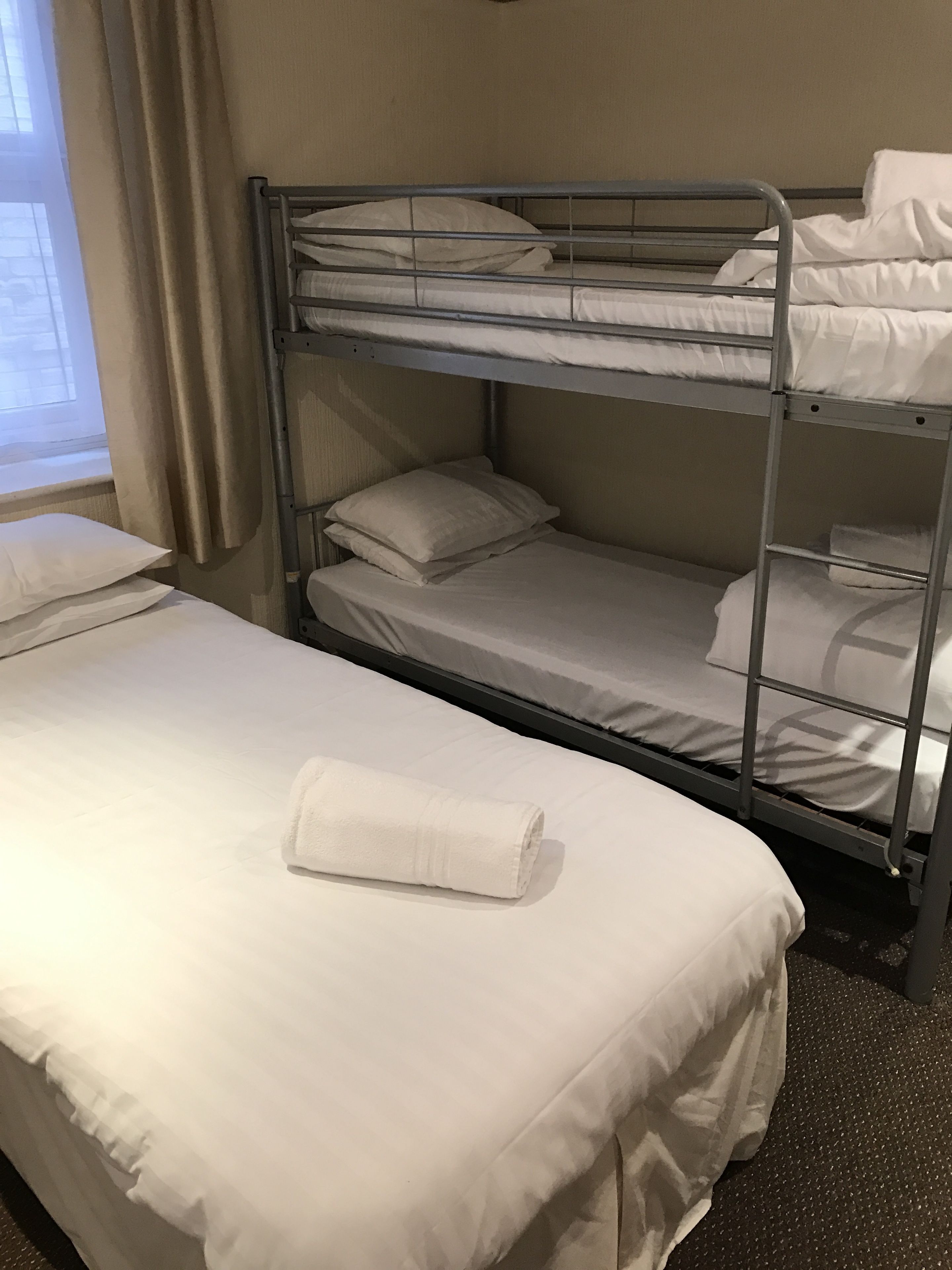A bunk bed with white bedding and a rolled towel on the lower bunk.