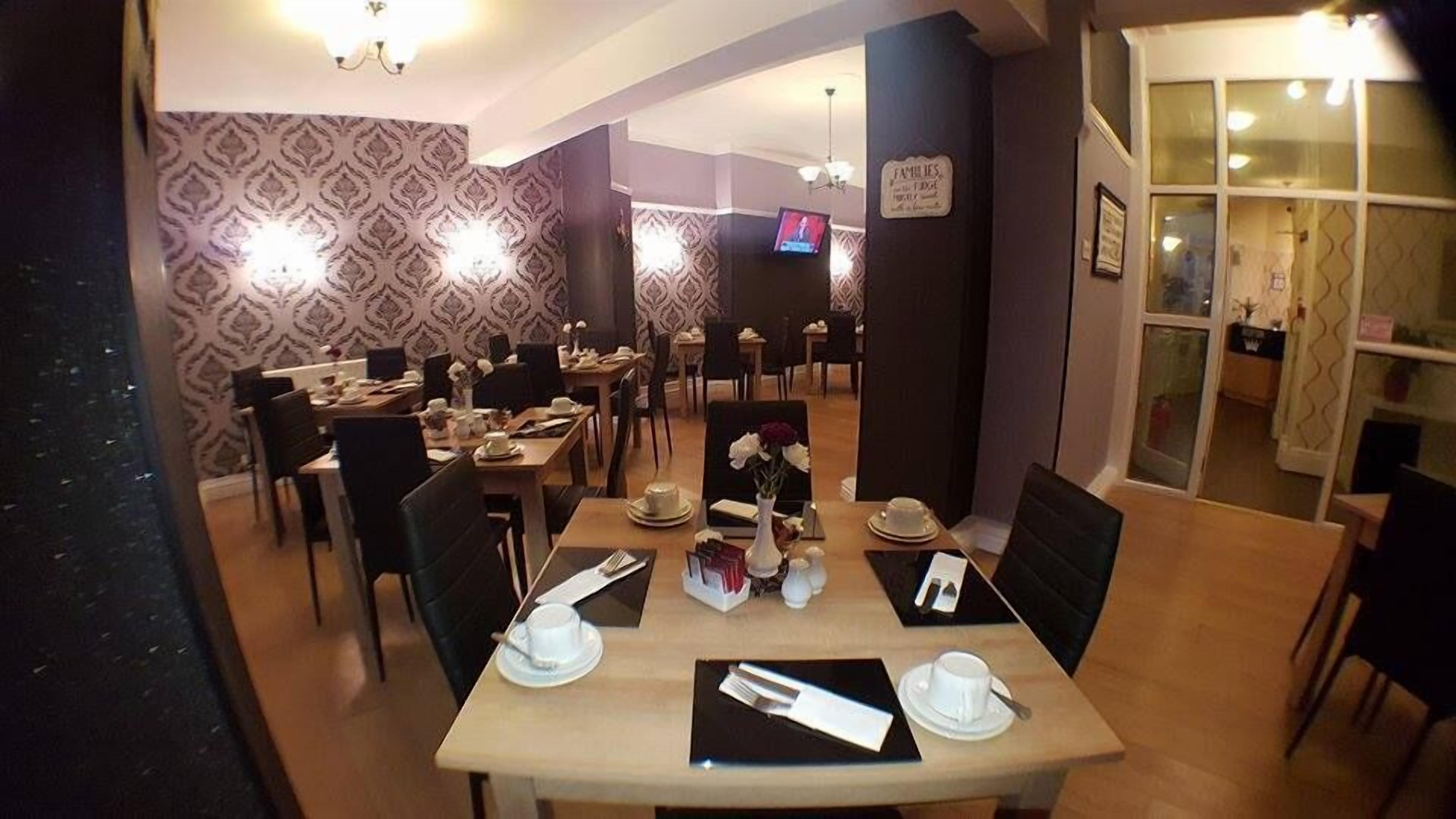 A dining area with multiple tables set for service, a television mounted on the wall, and patterned wallpaper.