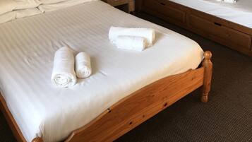 A hotel room with a single bed, a wooden headboard, a nightstand with a lamp, and a bunk bed with towels.