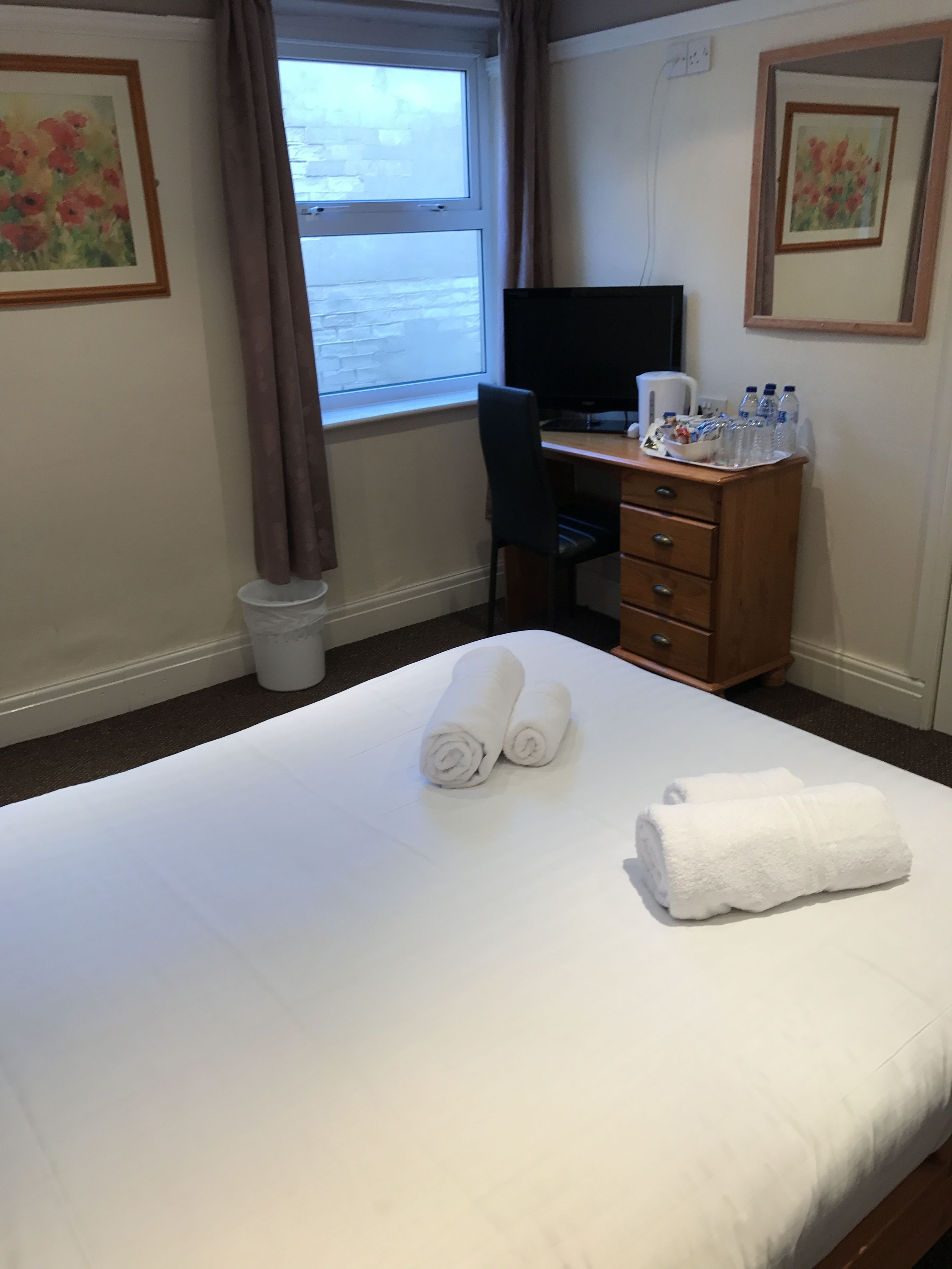 A hotel room with a bed, a desk, a chair, a television, and a window with curtains.