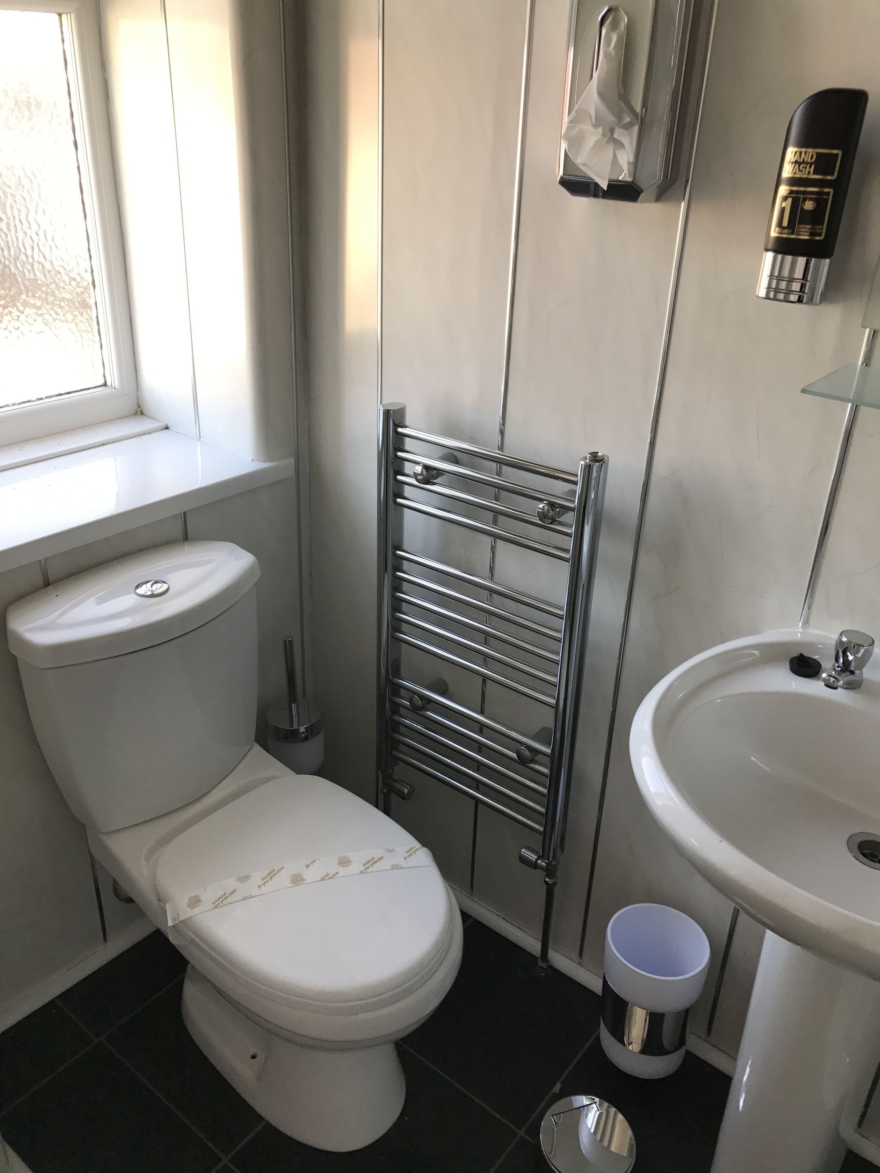 A bathroom with a toilet, a metal towel rack, a sink, and a window.