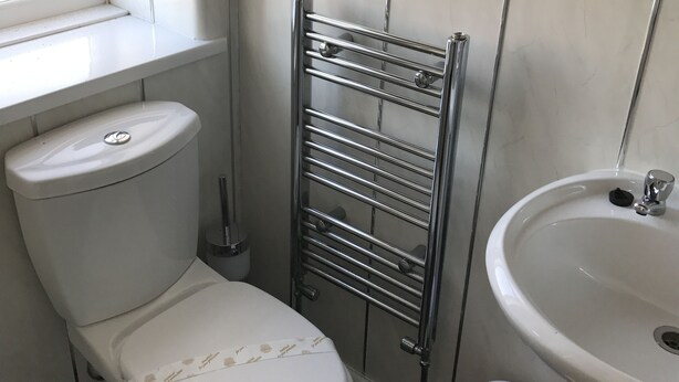 Un baño con inodoro, toallero metálico, lavamanos y ventana.