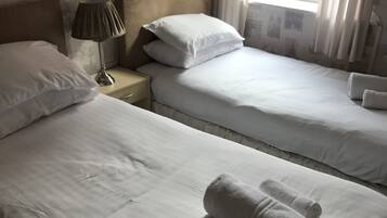 Habitación de hotel con dos camas, una mesita de noche con lámpara y una ventana con cortinas.