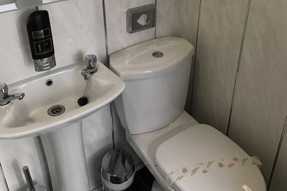 Une salle de bain avec un lavabo blanc, des toilettes et un point d’eau pour se laver les mains.