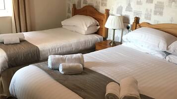 A hotel room with two beds, each with white linens and pillows, a wooden headboard, a bedside lamp, and a wall with a cityscape wallpaper.