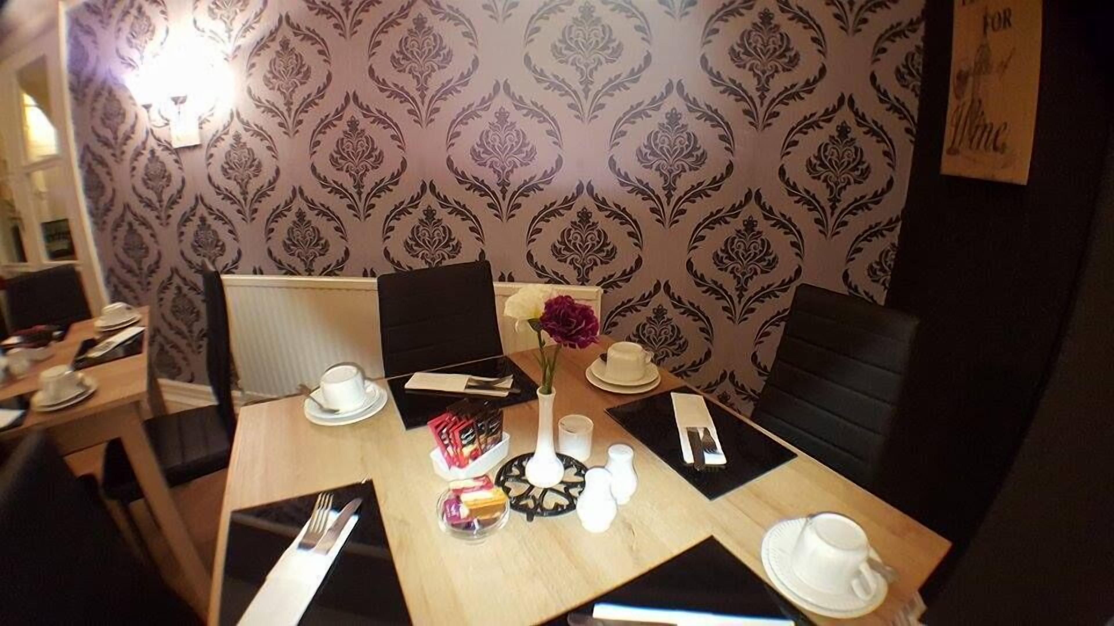 Un comedor con una mesa dispuesta para dos personas, con un florero con una sola flor, saleros y pimenteros, un cuenco pequeño de aperitivos y una taza con platillo.