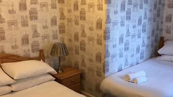 Ein Hotelzimmer mit zwei Betten, einem Nachttisch mit Lampe und einer Wand mit Paris-Motiven an der Tapete.