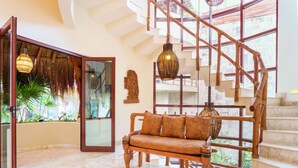 A spacious living area with a wooden bench, a staircase with a bamboo railing, and a large window offering a view of the outdoors.