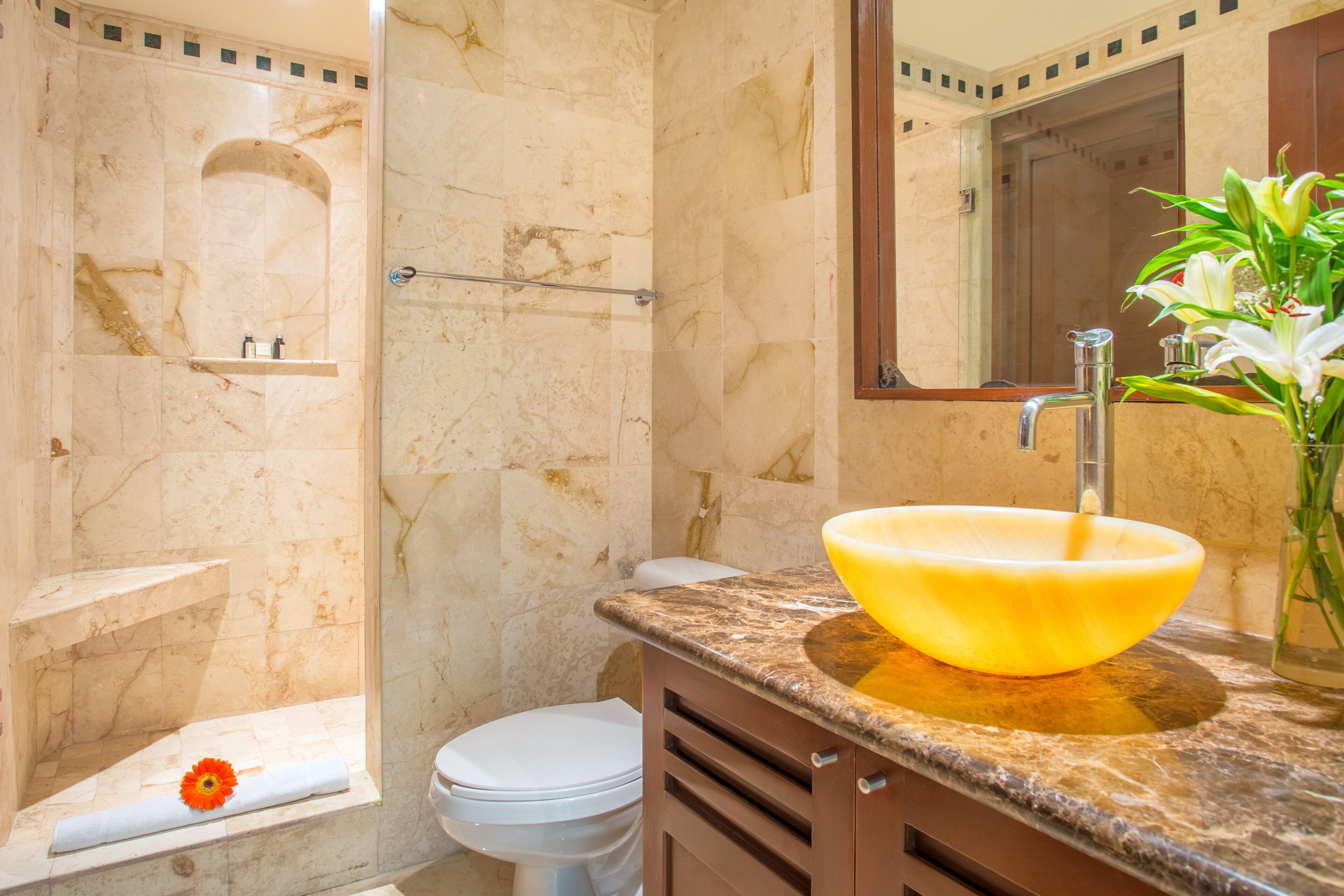 A bathroom with a marble wall, a white toilet, a yellow sink, and a shower area.