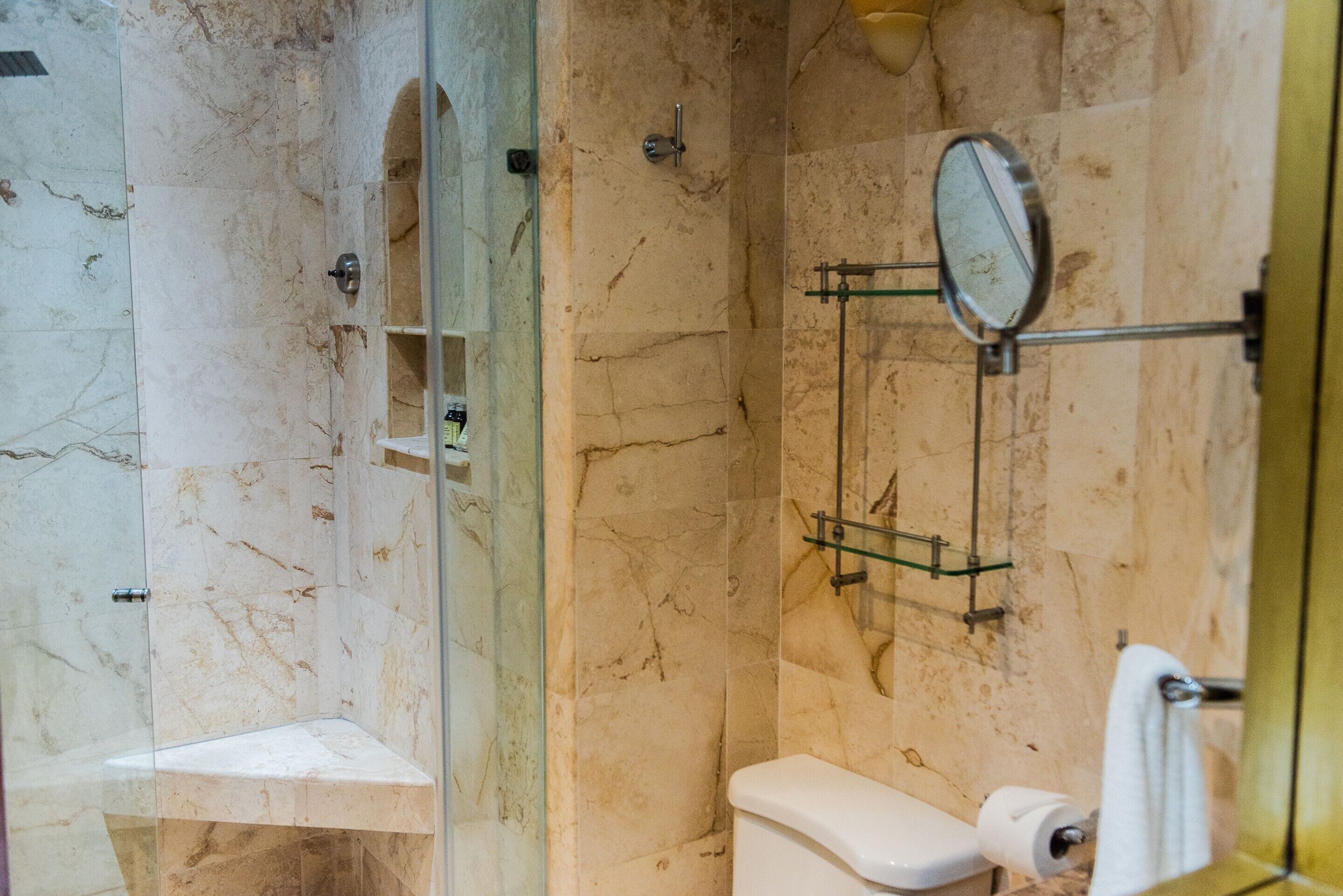 A bathroom with a glass-enclosed shower, a toilet, and a mirror on the wall.