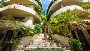 A hotel with a central staircase flanked by lush greenery and two-story buildings with balconies.