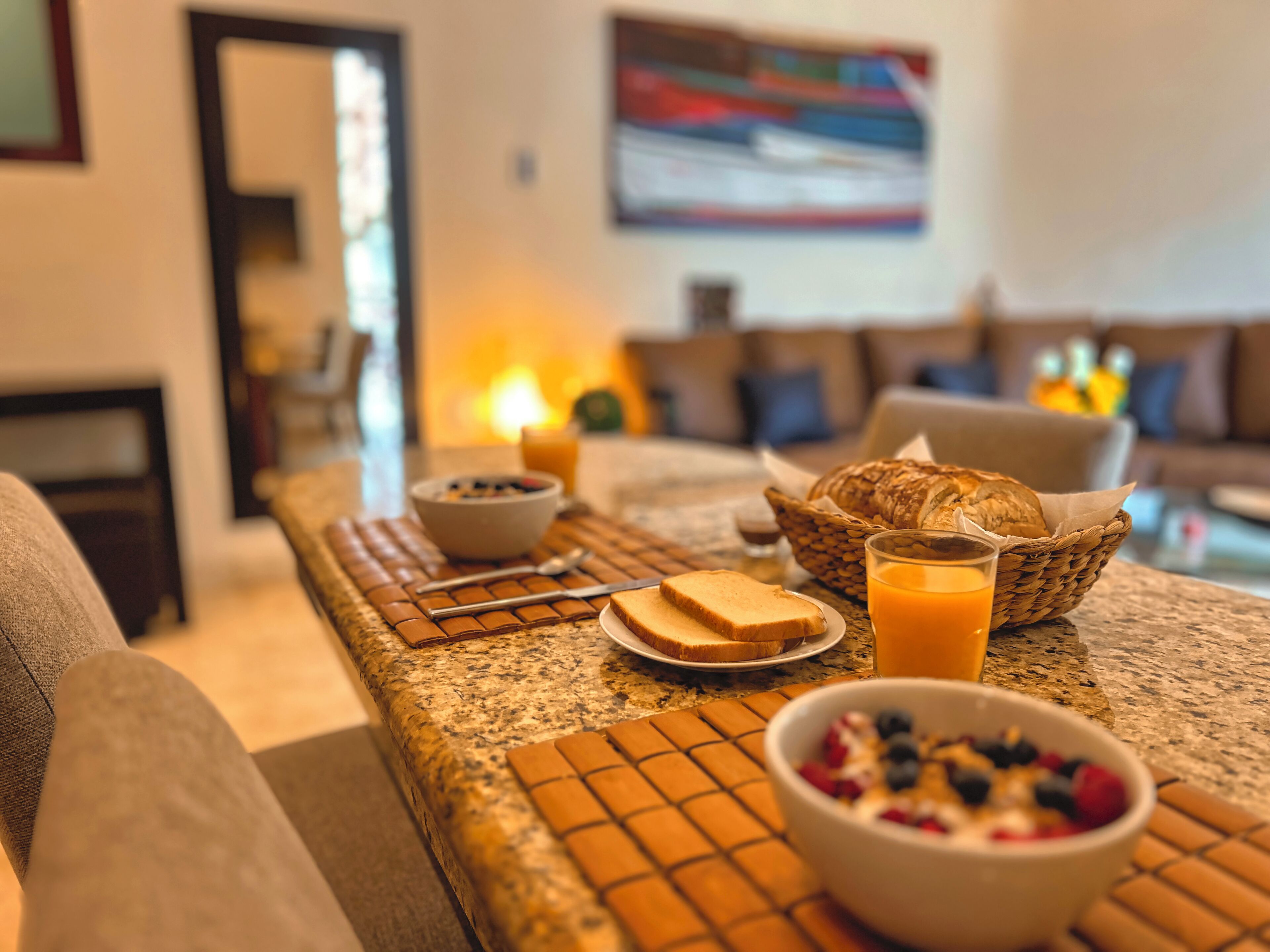 A breakfast setup with toast, cereal, and juice on a table in a living room with a sofa and a painting on the wall.