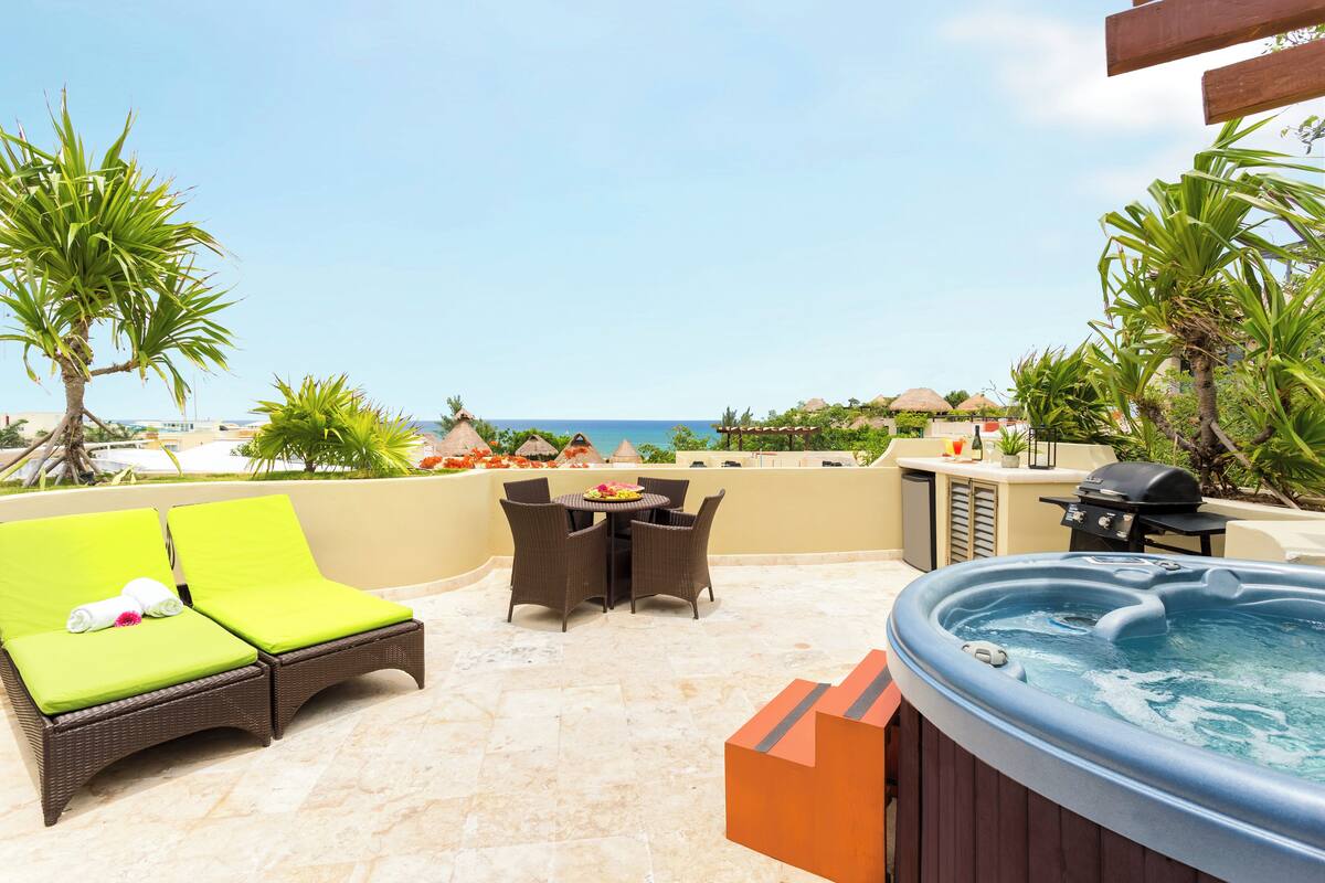 A patio with a hot tub, lounge chairs, and a table with chairs.