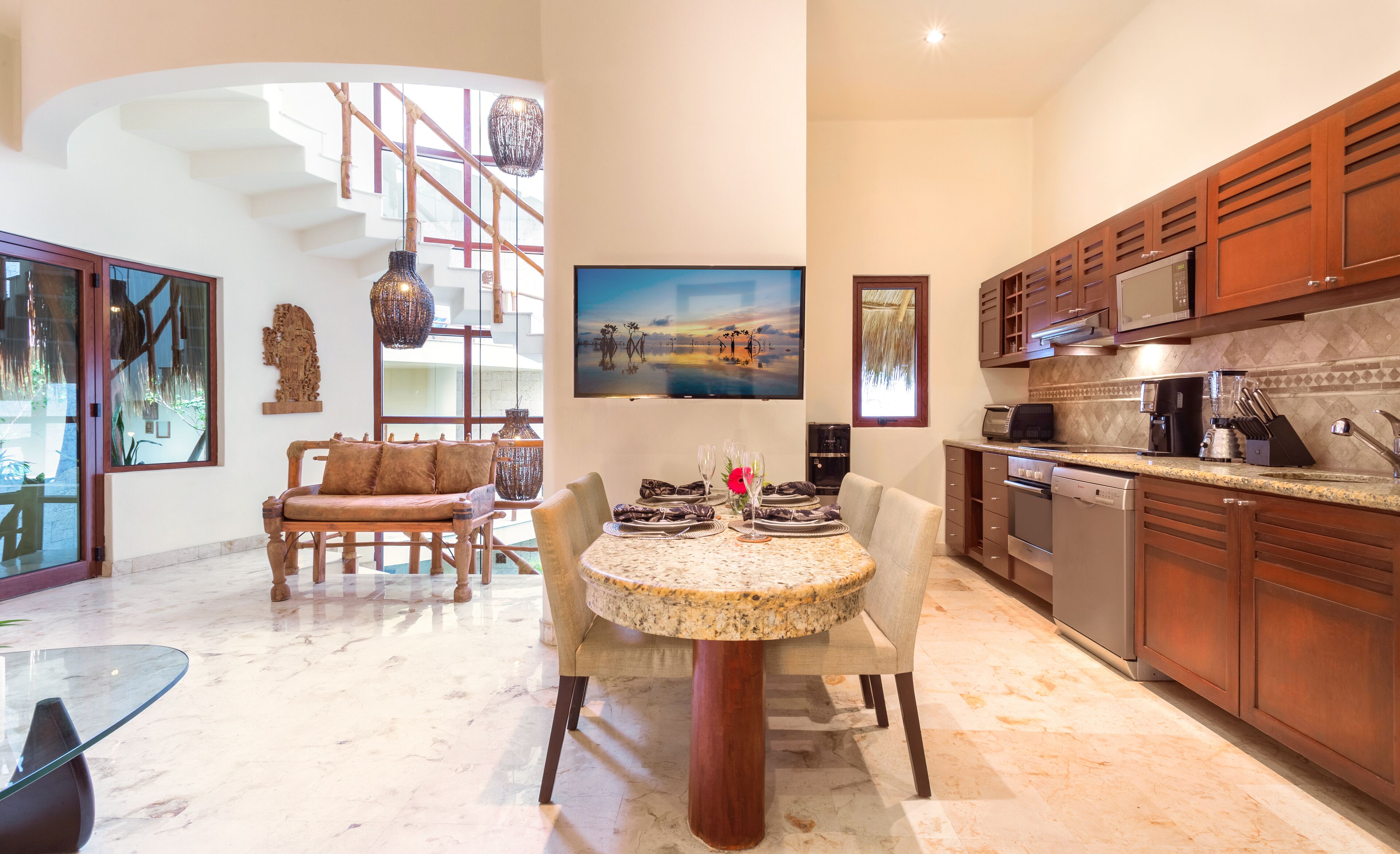 A spacious kitchen with modern appliances, a dining area with a round table, and a staircase with a unique design.