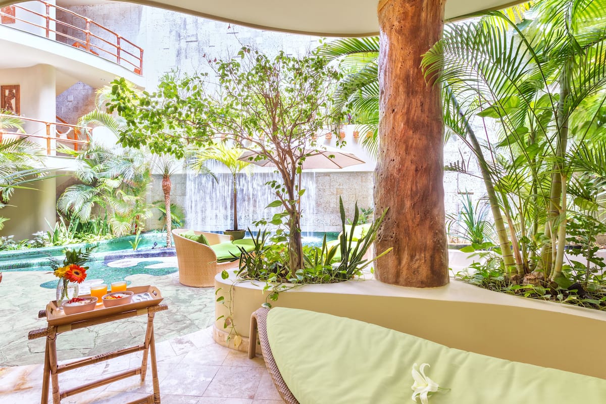 A lush indoor garden with a waterfall, a dining area with a table and chairs, and a large tree trunk.