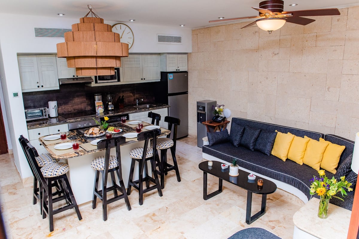 A modern kitchen with a dining area, a sofa, and a ceiling fan.