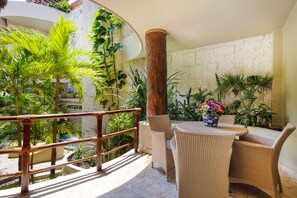 A sunlit outdoor seating area with wicker furniture, surrounded by lush tropical plants and a stone wall. - Maya Villa Condo Hotel & Beach Club (Playa del Carmen)
