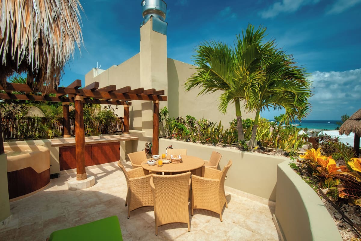 A patio with a round table and chairs, a pergola, and a view of the ocean.