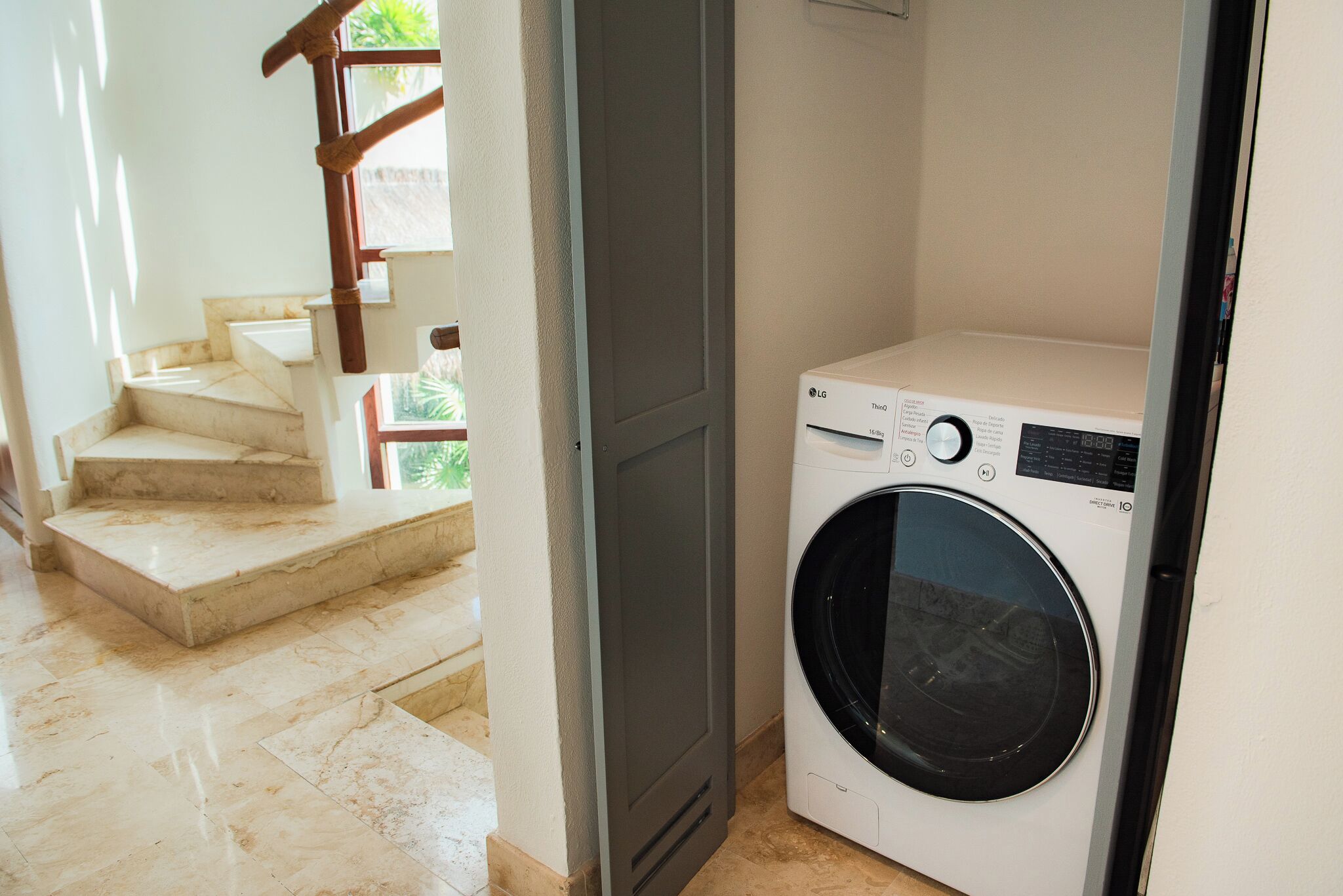 A laundry room with a front-loading washing machine, a staircase with marble steps, and a door leading to another room.