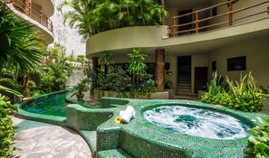 A spa area with a hot tub surrounded by lush greenery and a curved pool. - Maya Villa Condo Hotel & Beach Club (Playa del Carmen)
