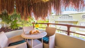 A balcony with wicker furniture, a table with pastries, and a hanging thatch ceiling.
