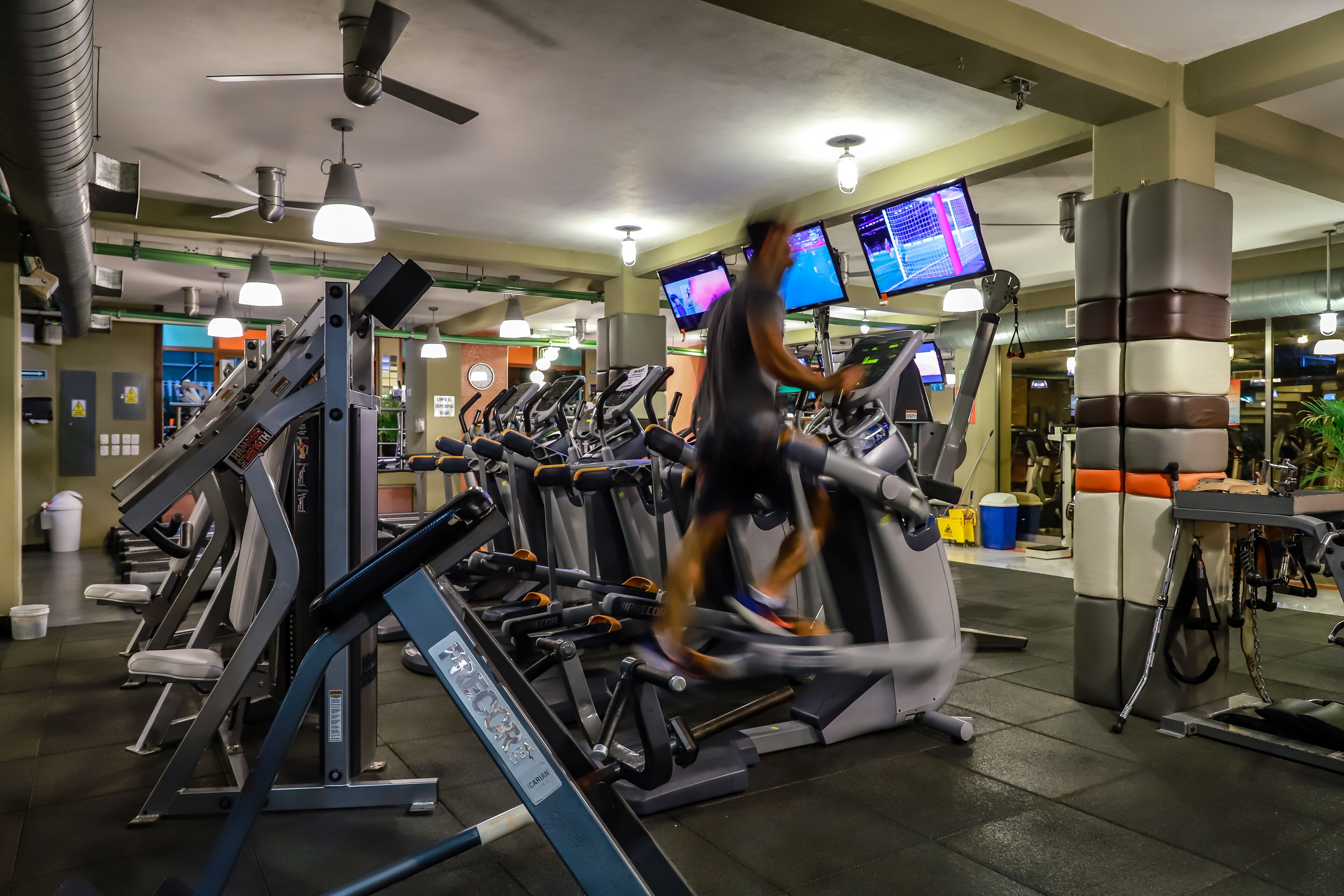 Une salle de sport équipée de plusieurs tapis de course, d’appareils d’exercice et d’écrans numériques affichant des informations sur les séances d’entraînement.