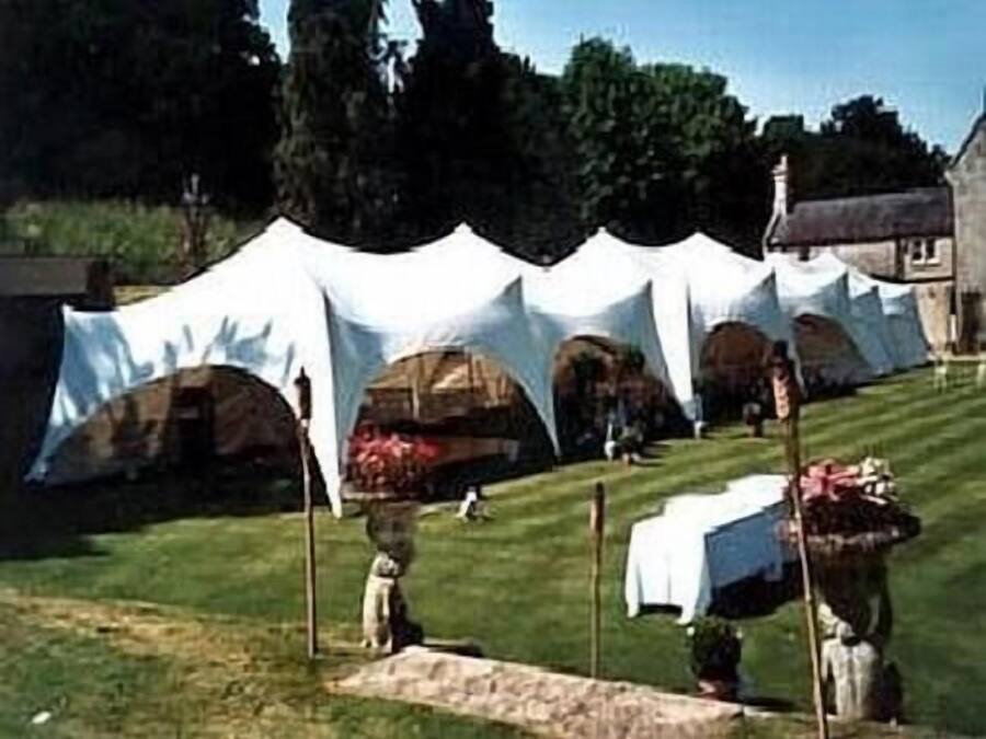 A tented outdoor area with a grassy lawn and a building in the background.