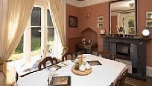 Een eetkamer met een tafel voor vier personen, een open haard en een grote spiegel aan de muur.