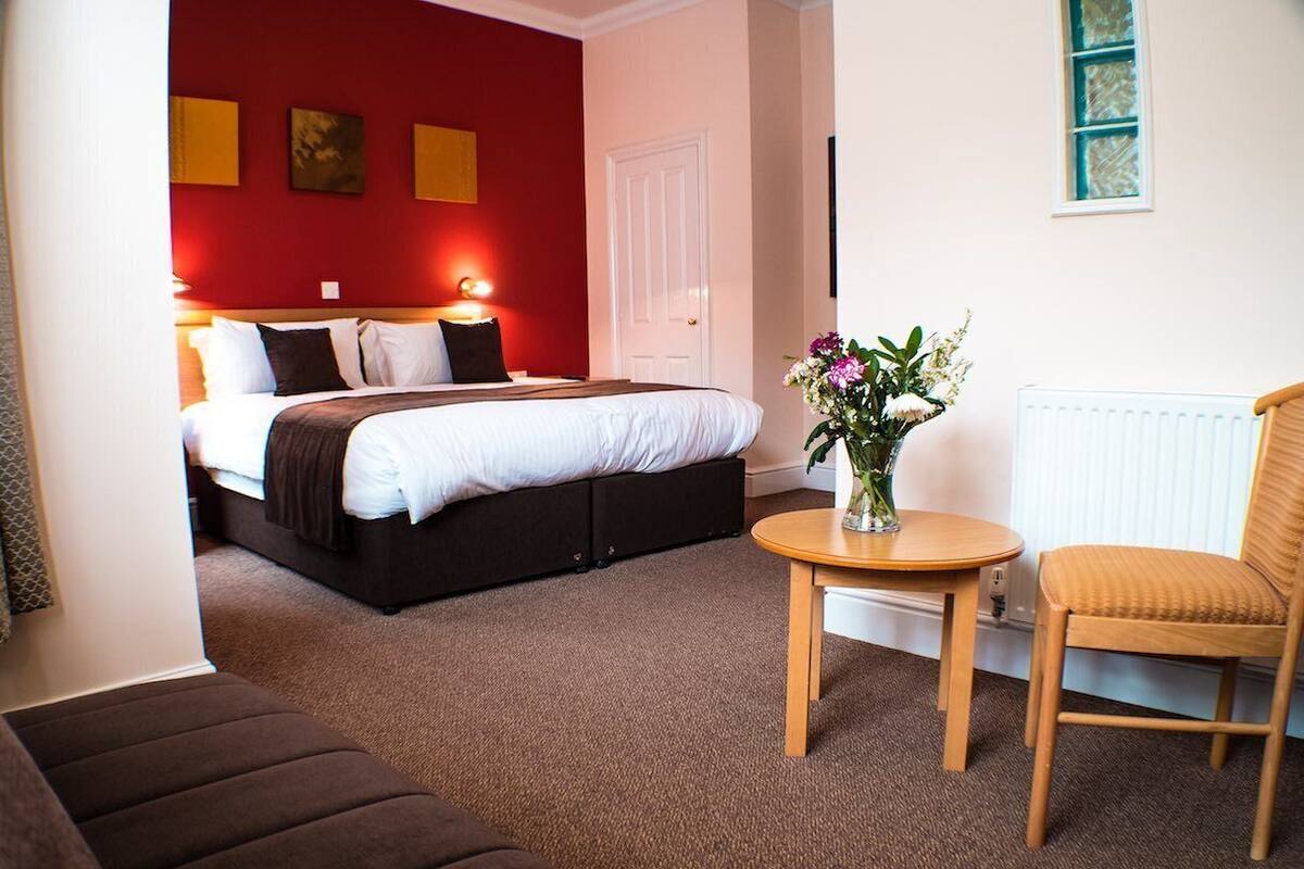 Una habitación de hotel con una cama, una mesita con un florero, una silla y un sofá.