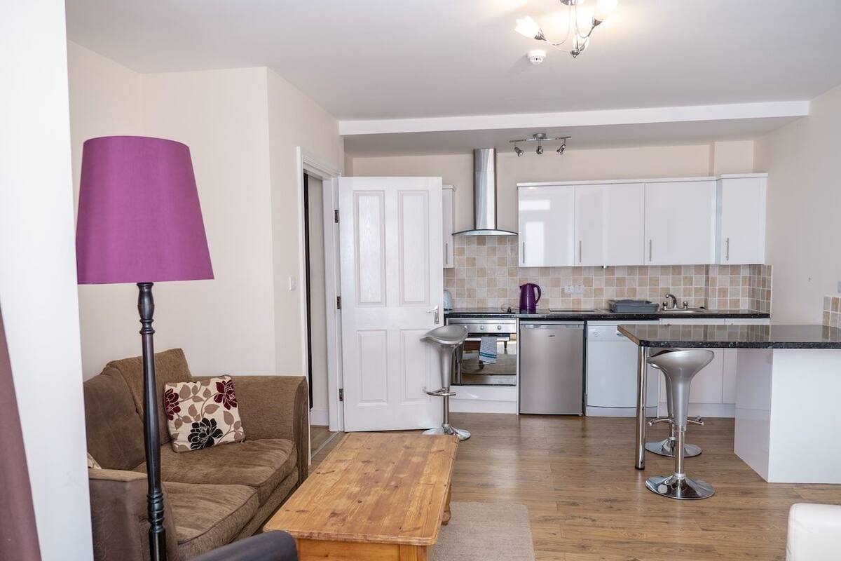 Una cocina moderna con armarios blancos, una mesa de comedor de madera y una lámpara de pie morada.