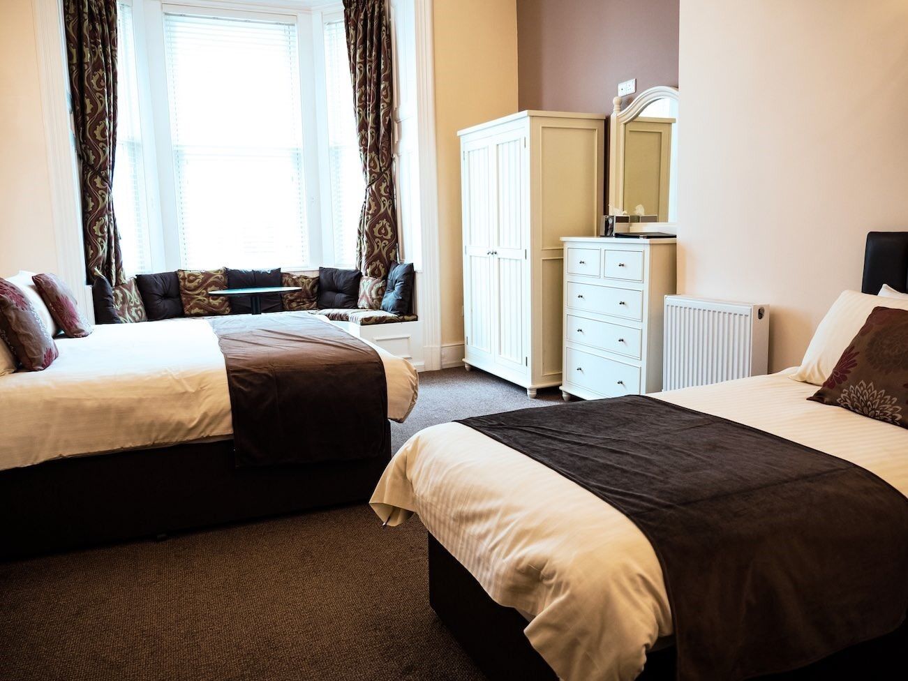 A hotel room with two beds, a wardrobe, a dresser, and a window with curtains.