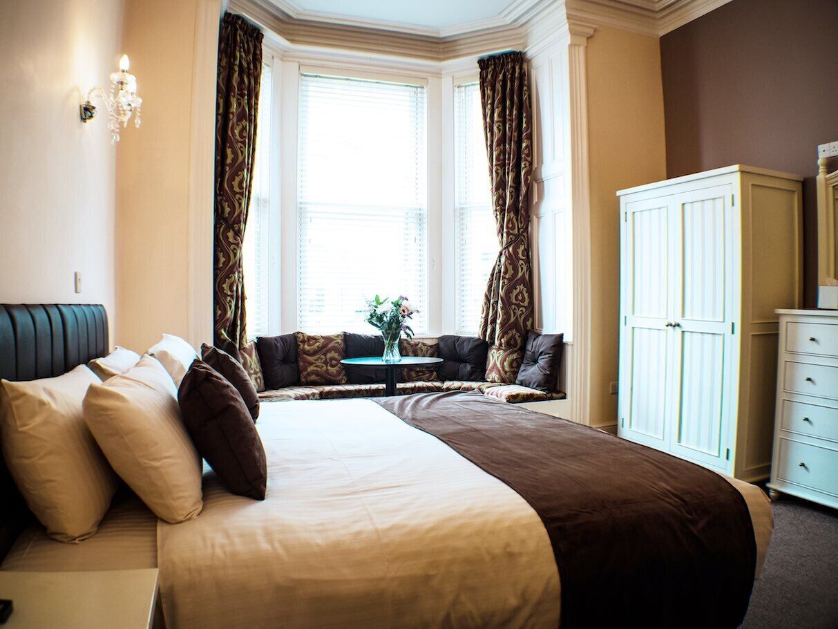 A hotel room with a large bed, a sofa, a small table with flowers, and a wardrobe.