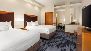 A hotel room with two beds, a desk, a television, and a bathroom visible in the background.