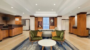 A lobby with a reception desk, two green sofas, a white coffee table, and a patterned carpet.