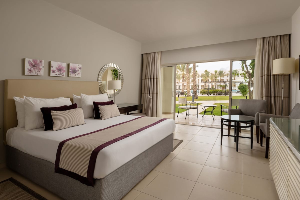 A hotel room with a large bed, a desk, and a view of a landscaped area.