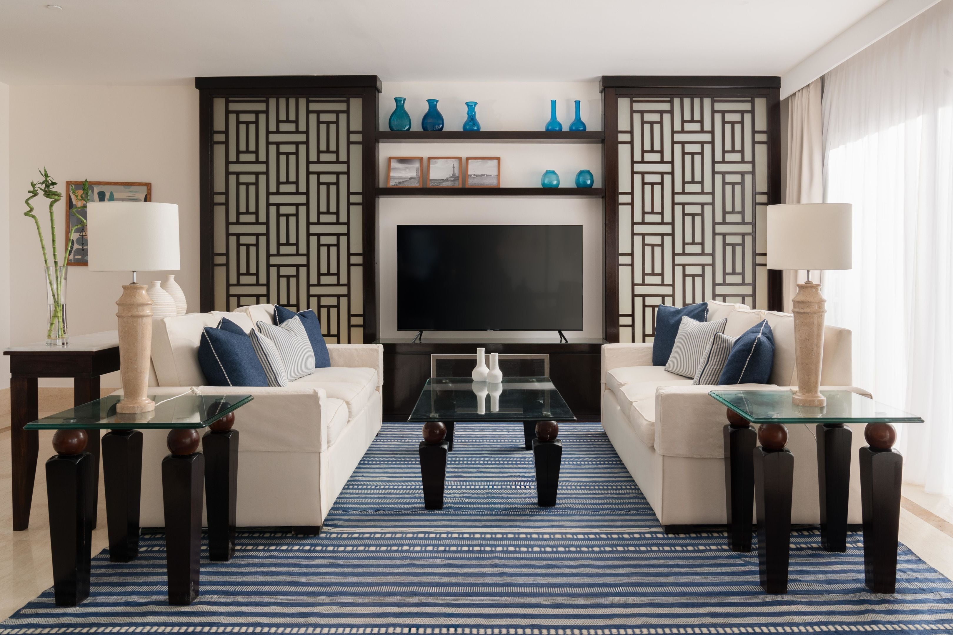 Ein Wohnzimmer mit zwei Sofas, einem Couchtisch, einem Fernseher, dekorativen Vasen und einer Wand mit Muster.