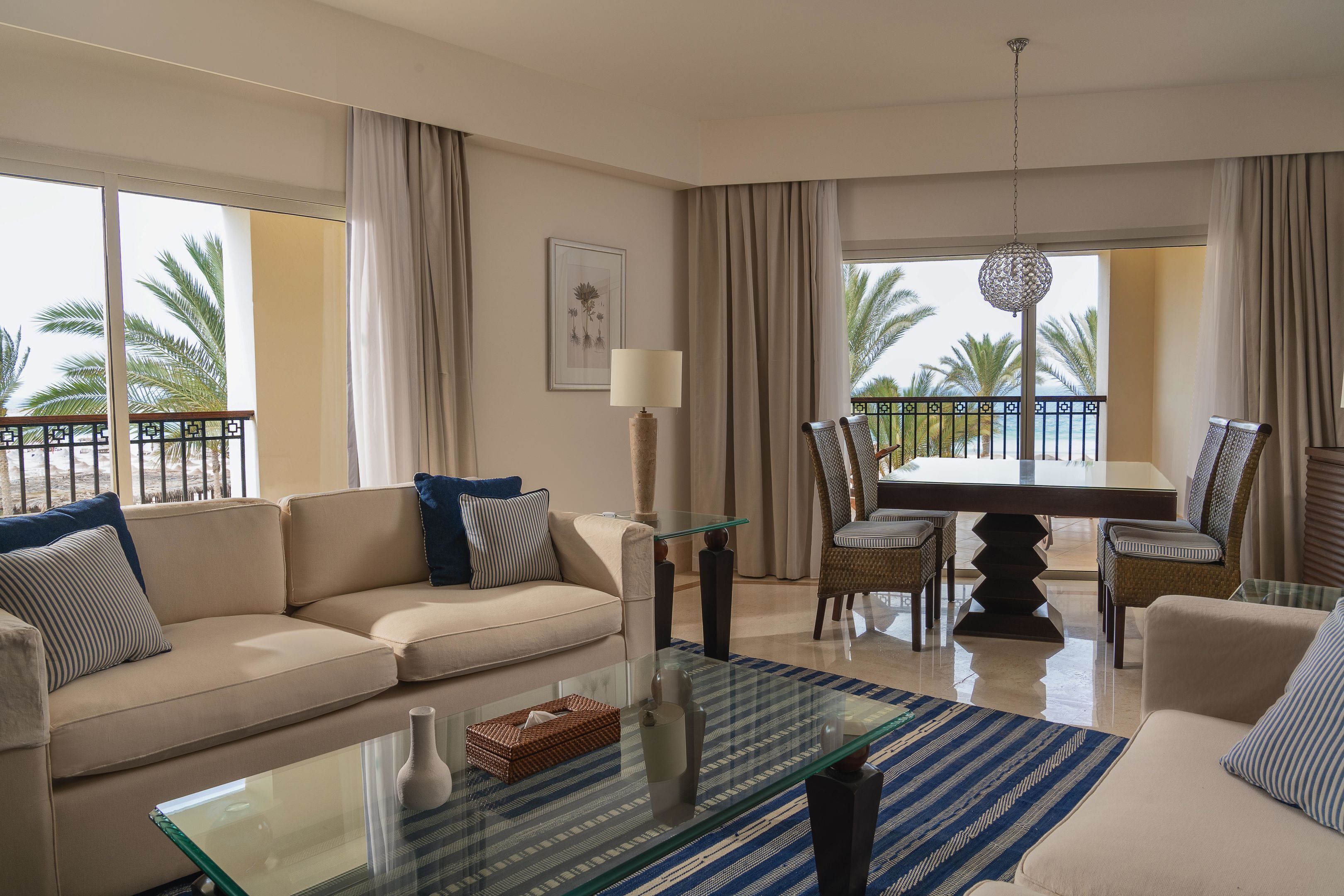 A living room with a sofa, coffee table, dining table, and chairs, with large windows and a balcony.