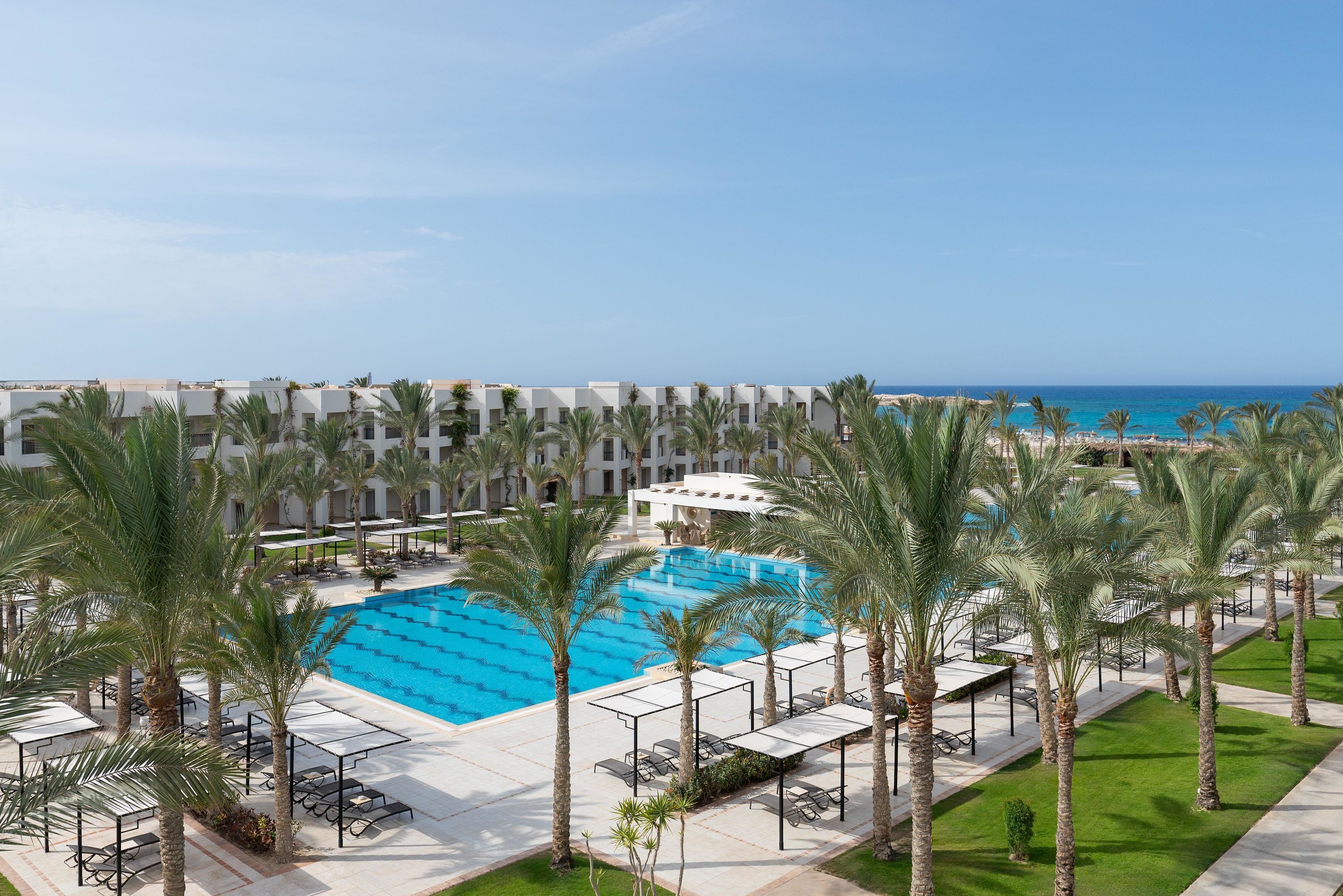 Un resort con una piscina grande, palmeras y vistas al océano.