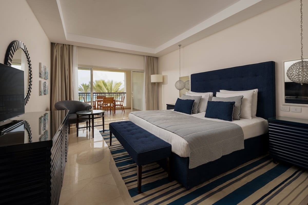 A modern hotel room with a large bed, a desk, and a balcony with a view.
